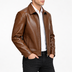 Brown - A man wearing a brown leather jacket over a white collared shirt and black jeans, shown from the waist up against a plain light gray studio background.
