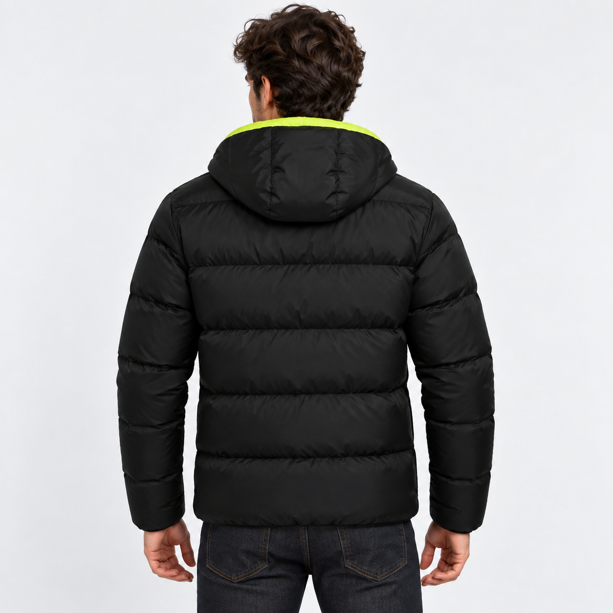 Green - A man viewed from behind wearing a black puffer jacket with a bright neon yellow-green hood lining, paired with dark blue jeans, against a light gray studio background.