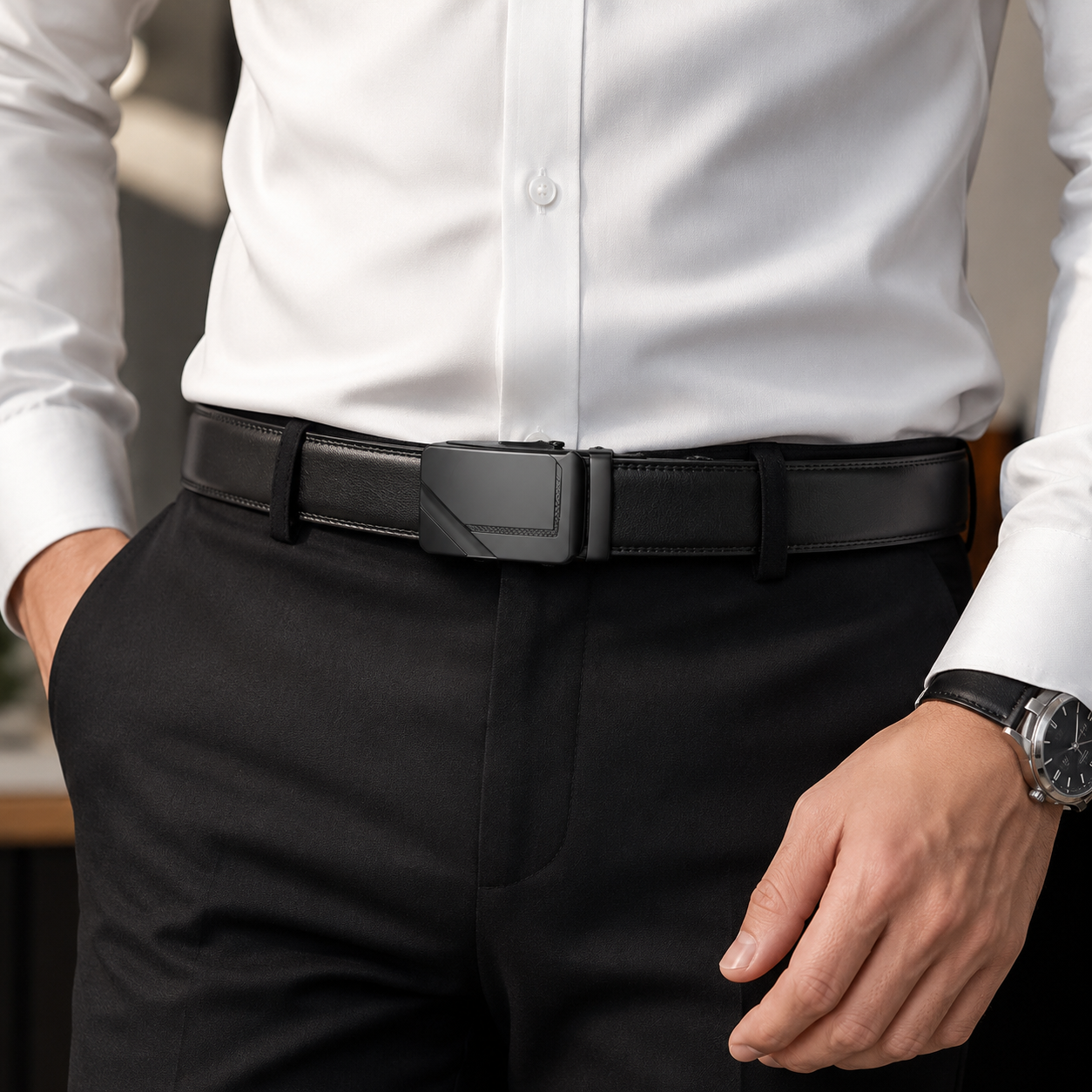 A close-up of a man wearing a black leather belt with a geometric, angular matte black buckle, styled with a white dress shirt and black trousers.