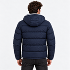 Navy Blue - A man viewed from behind wearing a navy blue hooded puffer jacket, paired with dark gray jeans, against a plain white studio background.