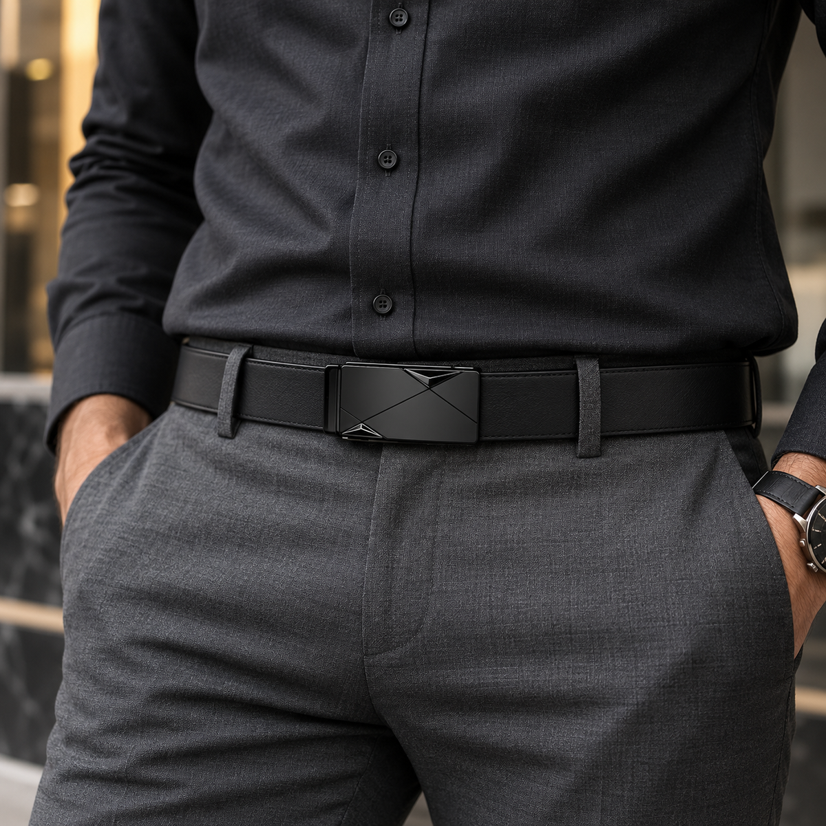 A close-up of a man wearing a black leather belt with a geometric metal buckle, paired with a dark charcoal dress shirt and gray trousers.