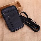 Black leather crossbody bag with a strap on a beige fabric background