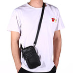 Person wearing a white t-shirt with a red and yellow logo, carrying a black crossbody bag.