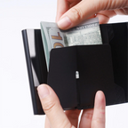 Hands inserting folded banknotes into the inner pocket of the open card holder.