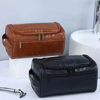 Brown and black leather toiletry bags on a white surface with a gray background