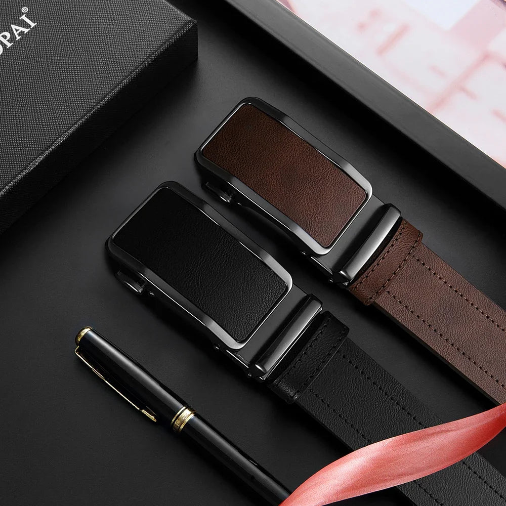 Two belts with black and brown buckles on a dark surface with a pen and gift box.