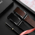Two belts with black and brown buckles on a dark surface with a pen and gift box.