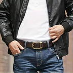 Person wearing a black leather jacket over a white shirt with blue jeans against a blurred brick wall background.