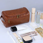 Brown leather toiletry bag with cosmetic items on a white background