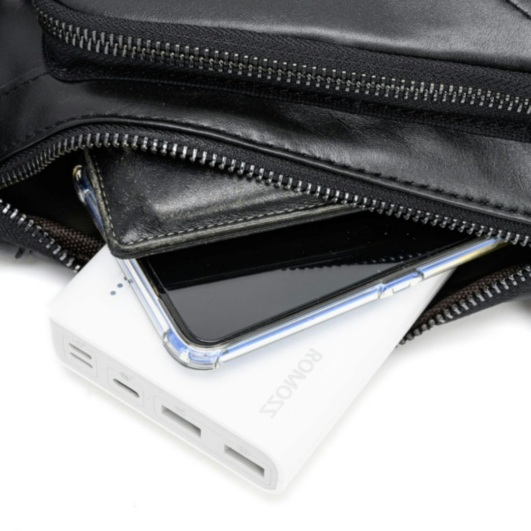 A close-up of a black leather zippered pouch with its zipper open, showing a white portable power bank and a smartphone tucked inside.