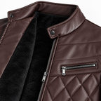 Brown - Close-up of a brown faux-leather jacket with a black sherpa lining, featuring a quilted chest panel, a zippered pocket, and a collar with a snap tab.