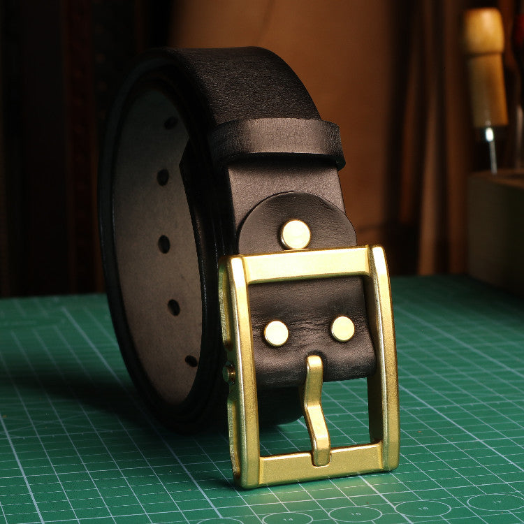 Brown leather belt with a gold buckle on a green cutting mat.